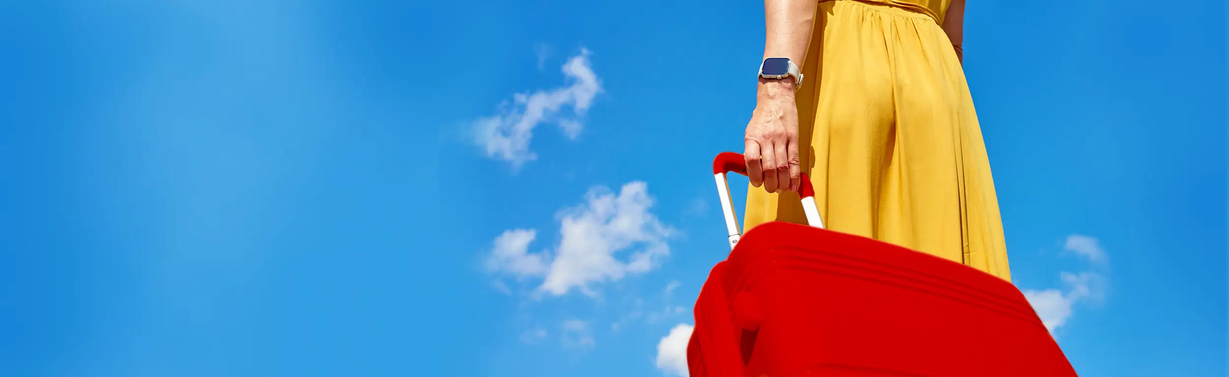 A person in a yellow dress holding a bright red suitcase against a clear blue sky.